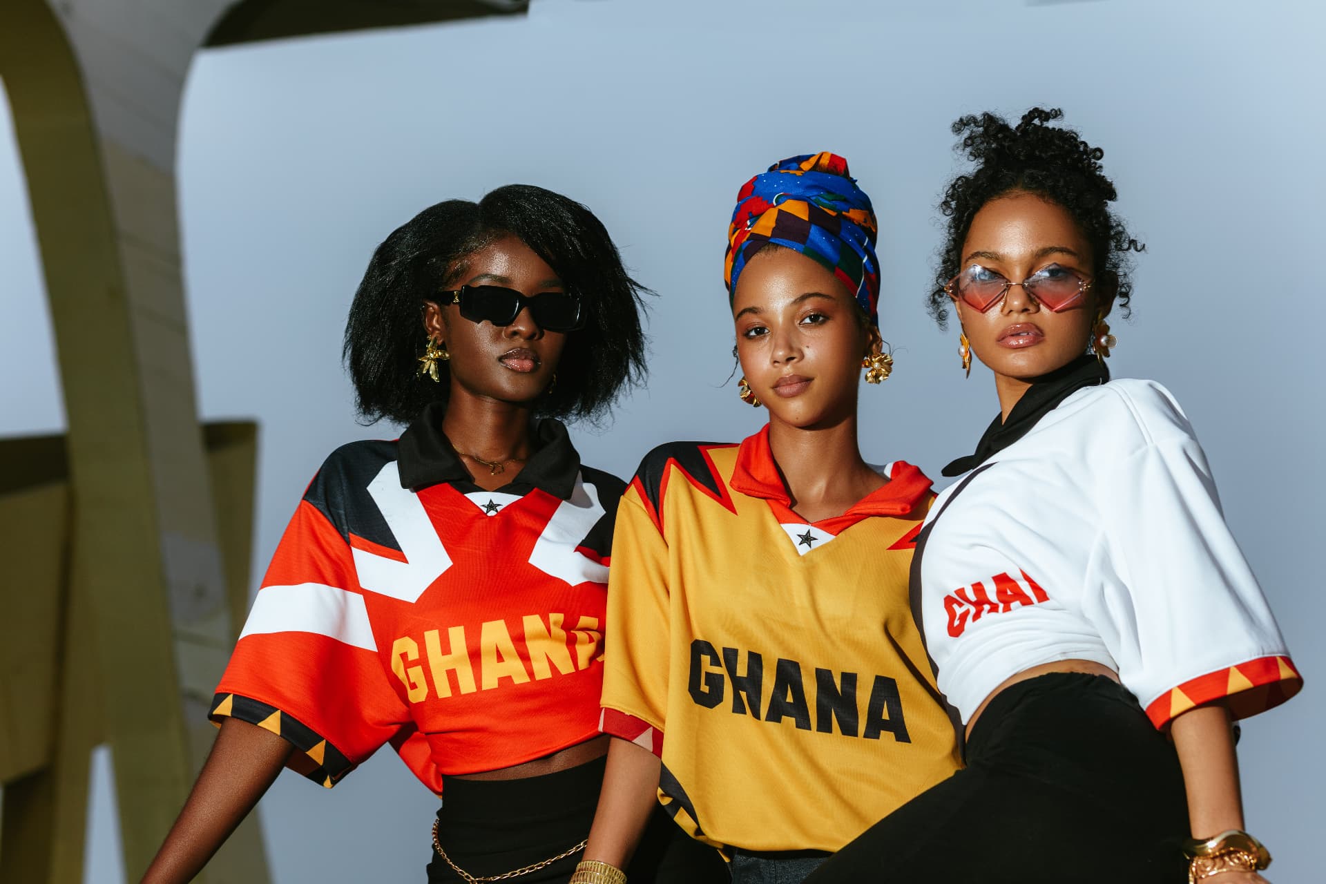 Three models wearing bold Ghana-inspired jerseys in red, gold and white